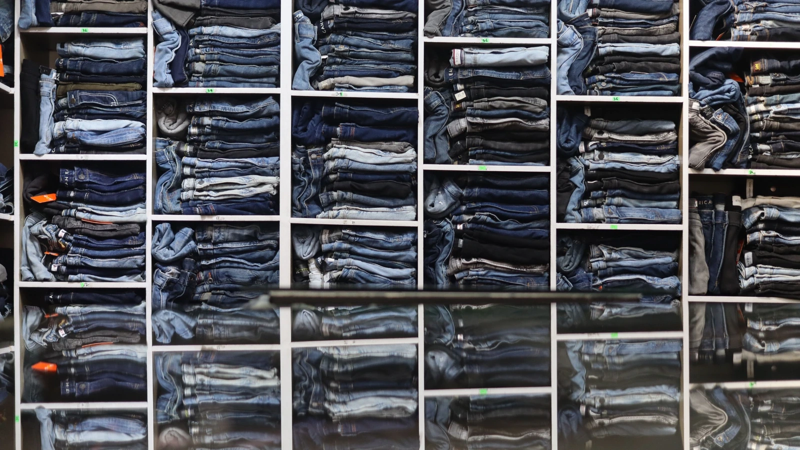 Pilas de vaqueros de denim doblados en estanterías de una tienda.